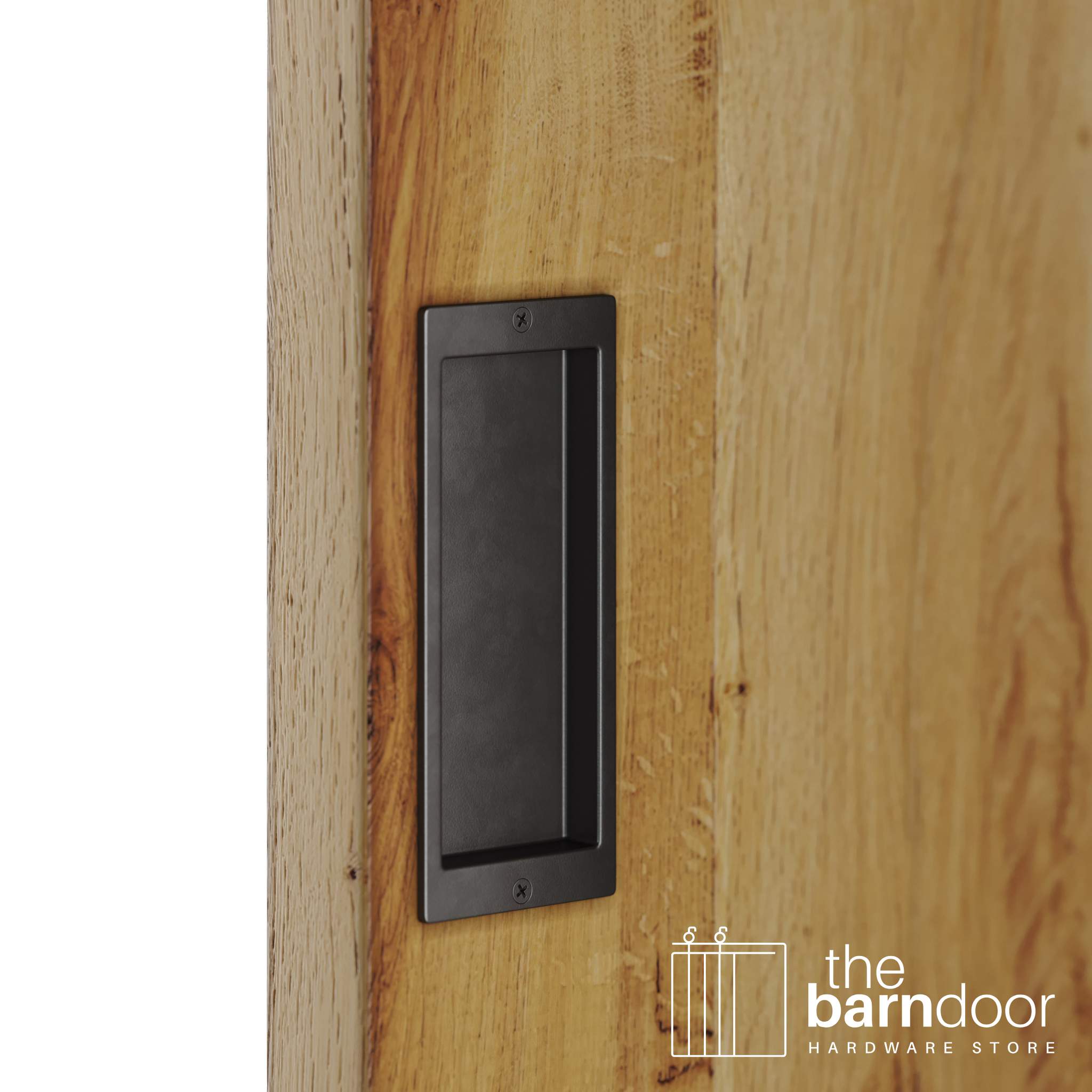 A close-up shot of a recessed rectangular flush pull handle in an arch bronze finish, installed on a light brown wooden barn door.