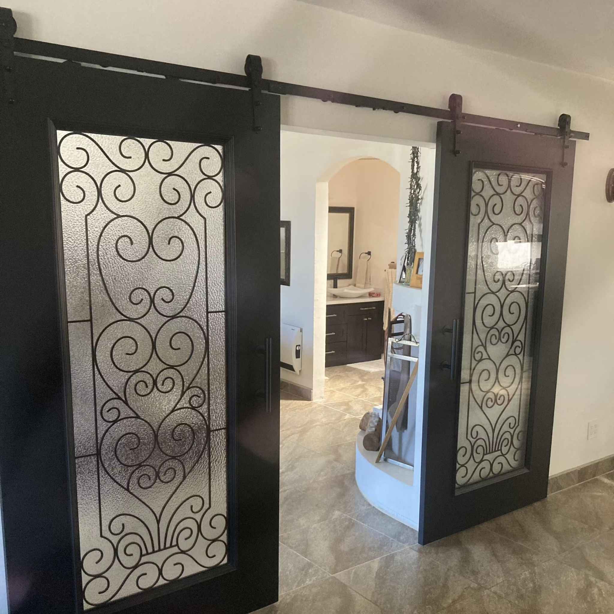 A customer install of a Arrow Single Track barn door hardware kit in a matte black finish, shown on a black wooden double barn doors with glass panels.