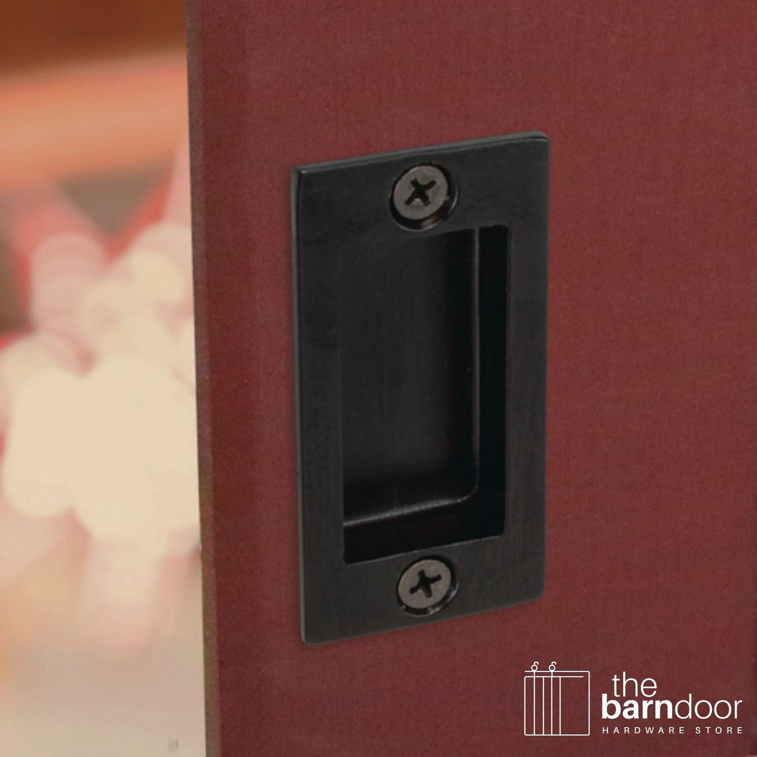 A close-up shot of a recessed rectangular flush pull handle in a black finish, installed on a red wooden barn door.