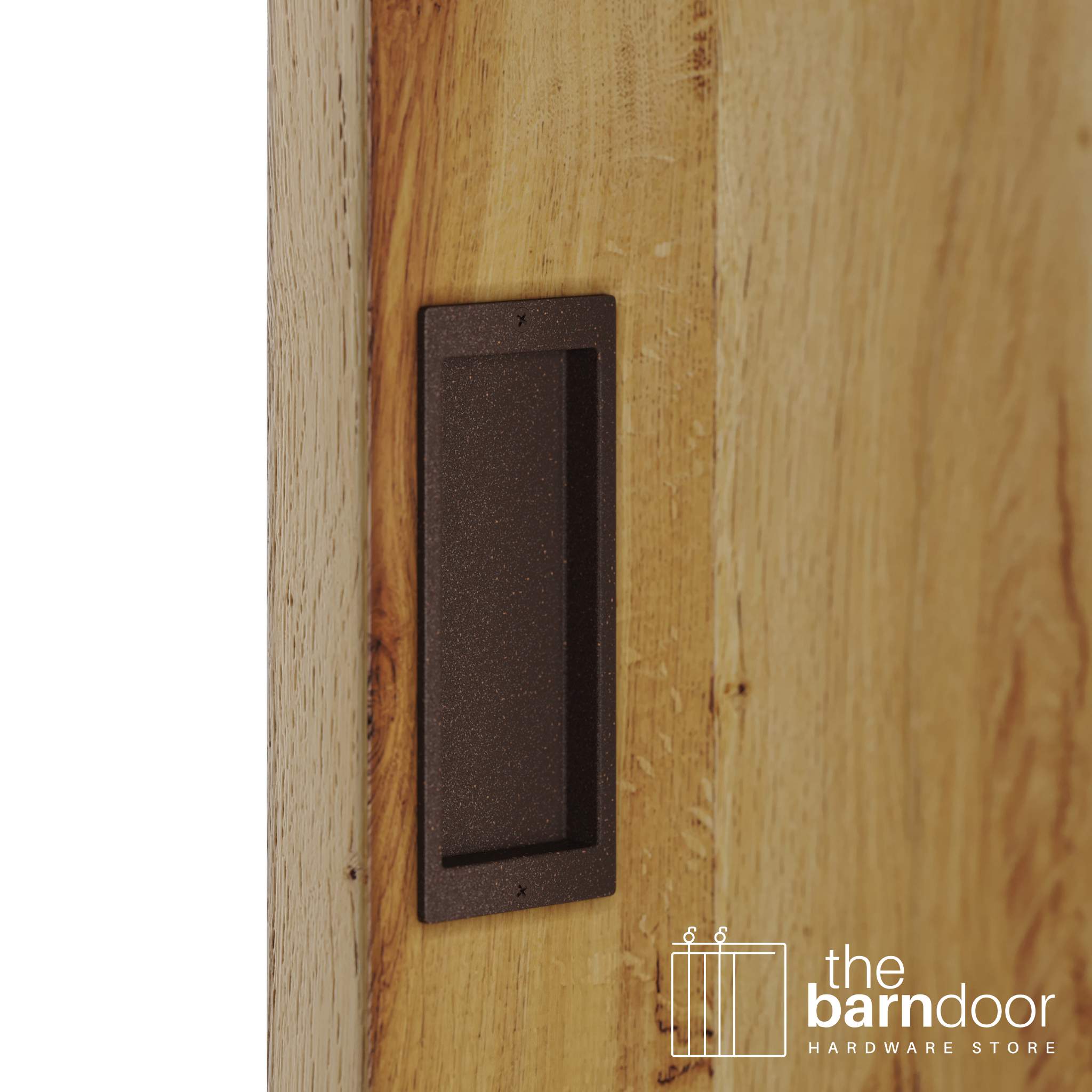 A close-up shot of a recessed rectangular flush pull handle in a bronze, textured finish, installed on a light brown wooden barn door.