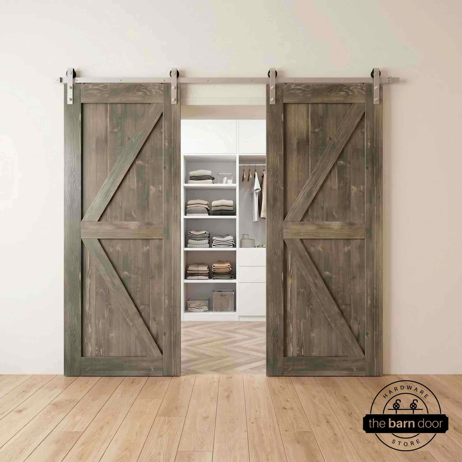 Two wood double barn doors with a two-panel vertical plank design in a Classic Gray stain, installed with brushed nickel sliding hardware, partially revealing a living room area.