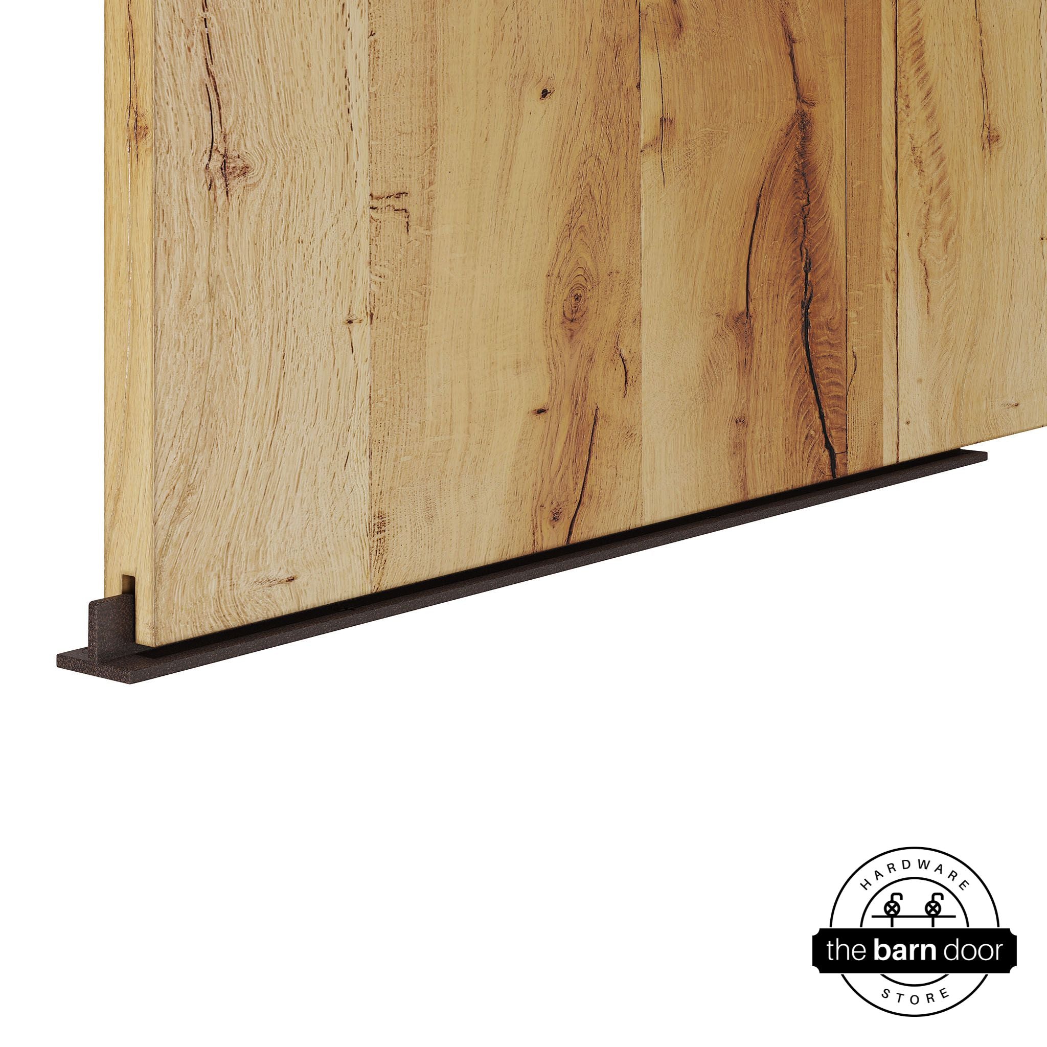 Copper Vein continuous T-guide floor track for barn doors by The Barn Door Hardware Store. Close-up of a heavy-duty bottom floor guide installed on a rustic wood door for stabilization and smooth sliding operation.