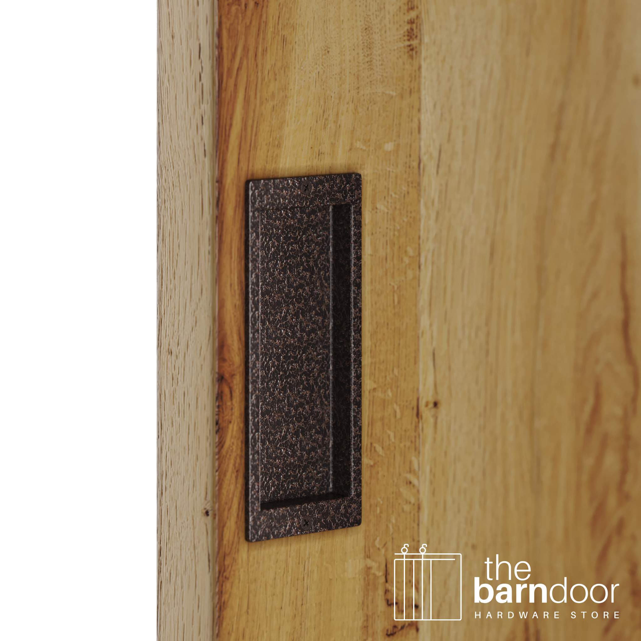 A close-up shot of a recessed rectangular flush pull handle in a copper vein, textured finish, installed on a light brown wooden barn door.