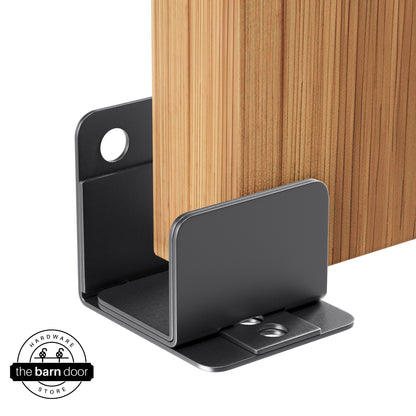 A dark gray U-shaped floor guide with a side plate, holding a light wood barn door in place.