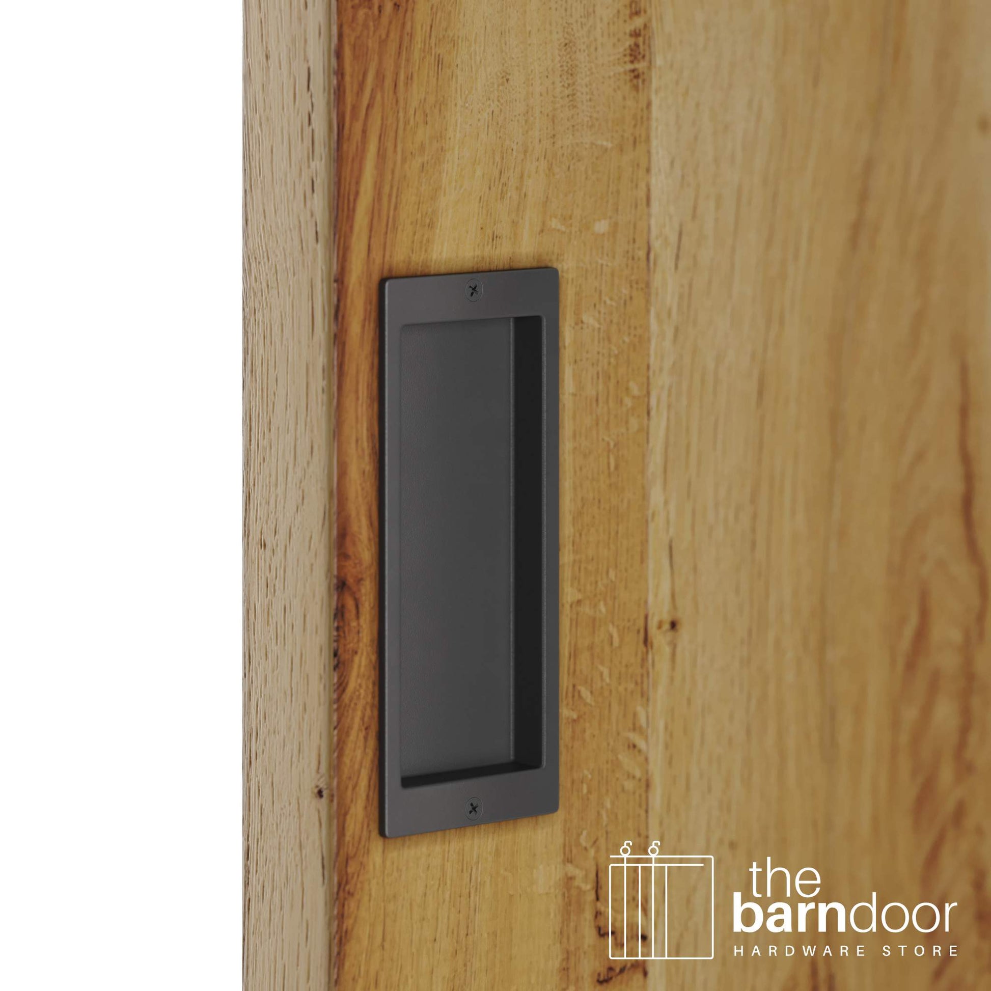A close-up shot of a recessed rectangular flush pull handle in a dark gray finish, installed on a light brown wooden barn door.