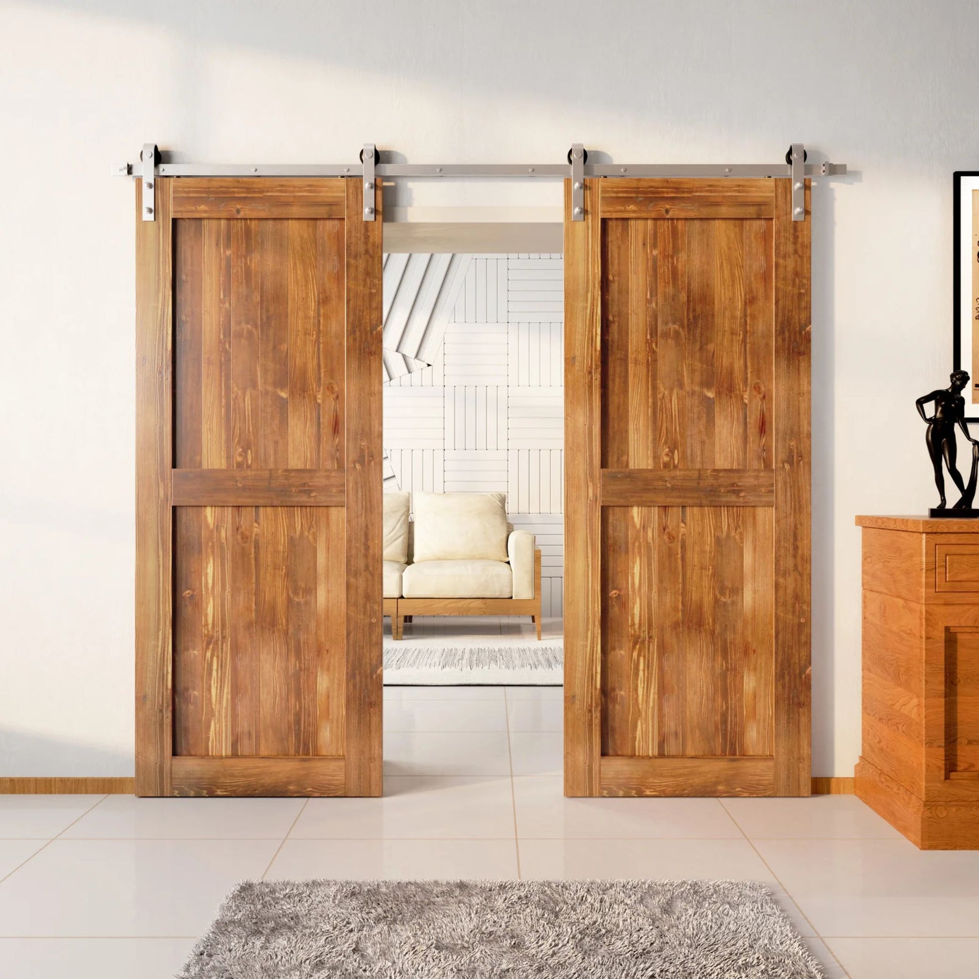 Two wood double barn doors with a two-panel vertical plank design in a light, golden Early American stain, installed with brushed nickel sliding hardware, partially revealing a living room area.