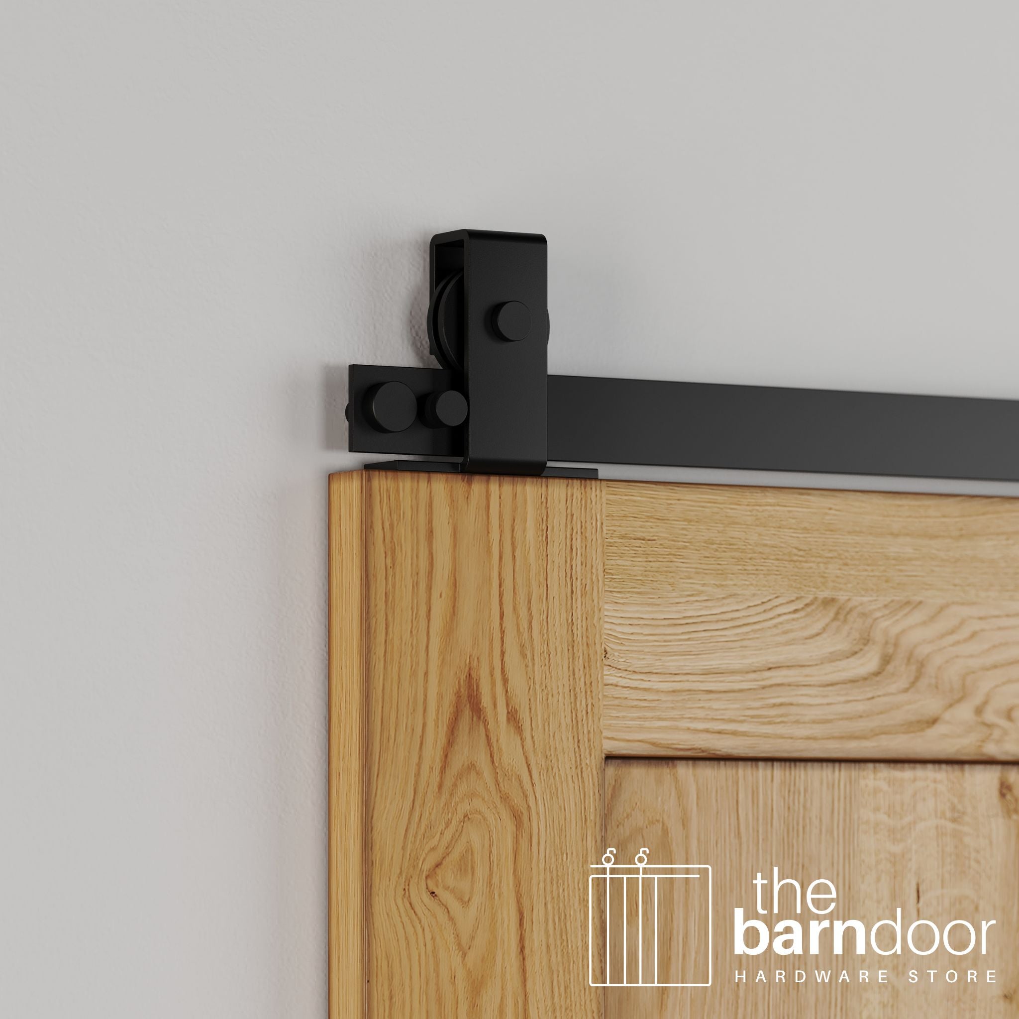 Close-up of Black Stainless Steel Flat Top Mount barn door hardware installed on the top edge of a natural oak wood door, showing the minimalist roller design.