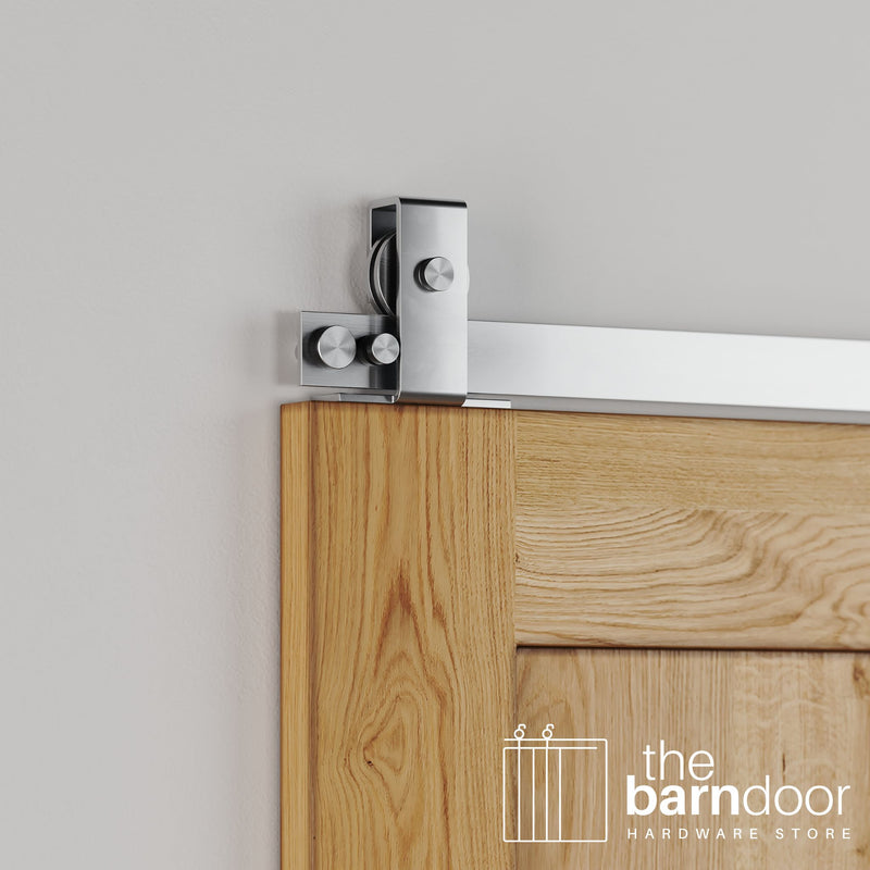 Close-up of Stainless Steel Flat Top Mount barn door hardware installed on the top edge of a natural oak wood door.