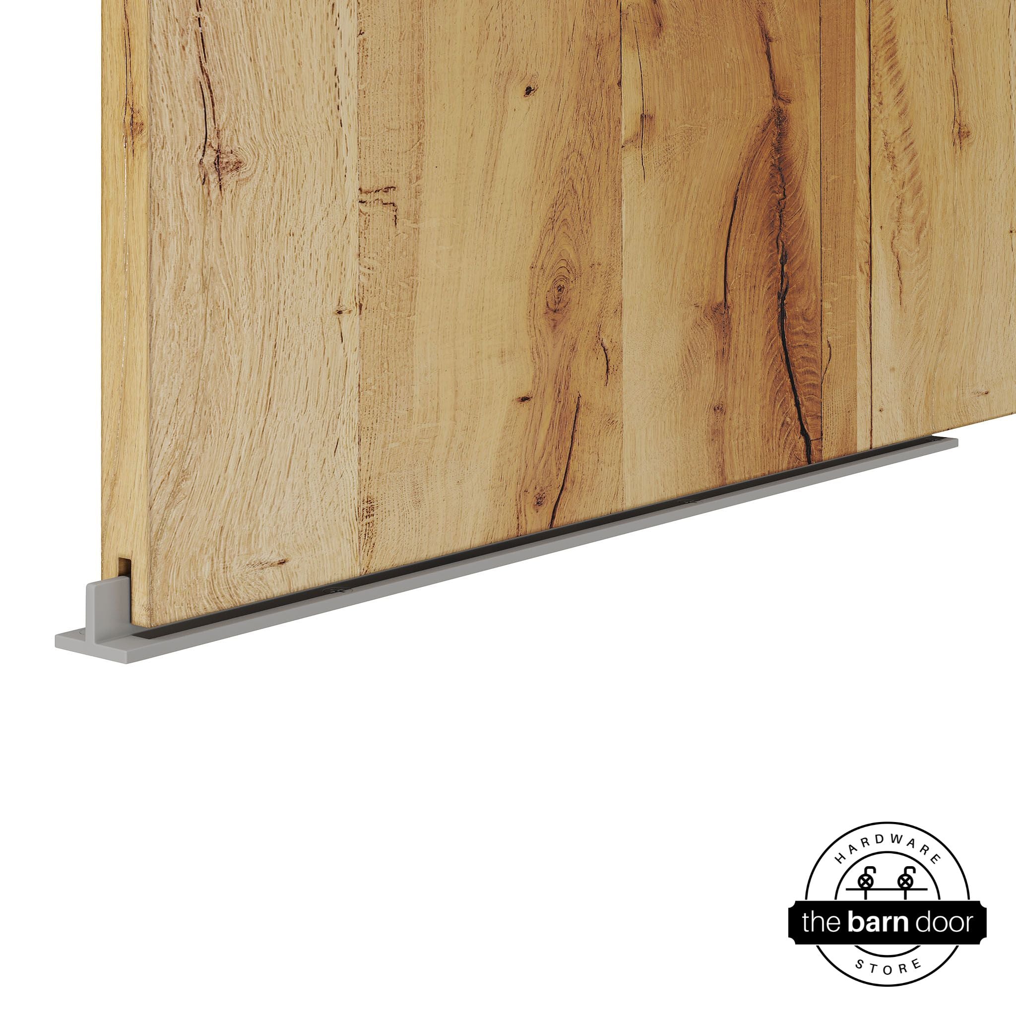 Flint Gray continuous T-guide floor track for barn doors by The Barn Door Hardware Store. Close-up of a heavy-duty bottom floor guide installed on a rustic wood door for stabilization and smooth sliding operation.