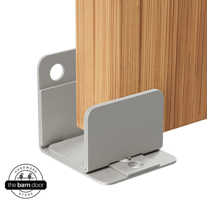 A flint gray U-shaped floor guide with a side plate, holding a light wood barn door in place.