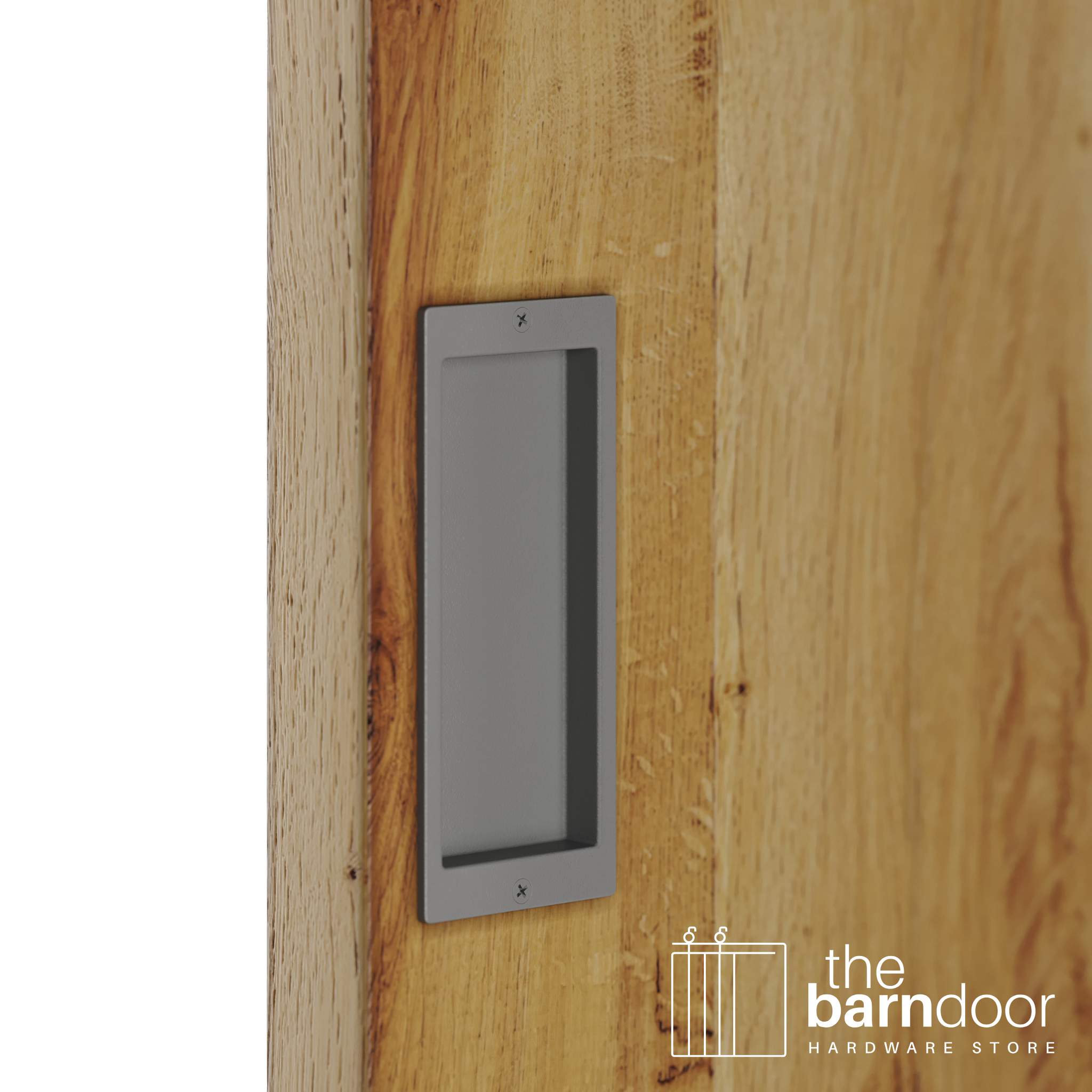 A close-up shot of a recessed rectangular flush pull handle in a flint gray finish, installed on a light brown wooden barn door.
