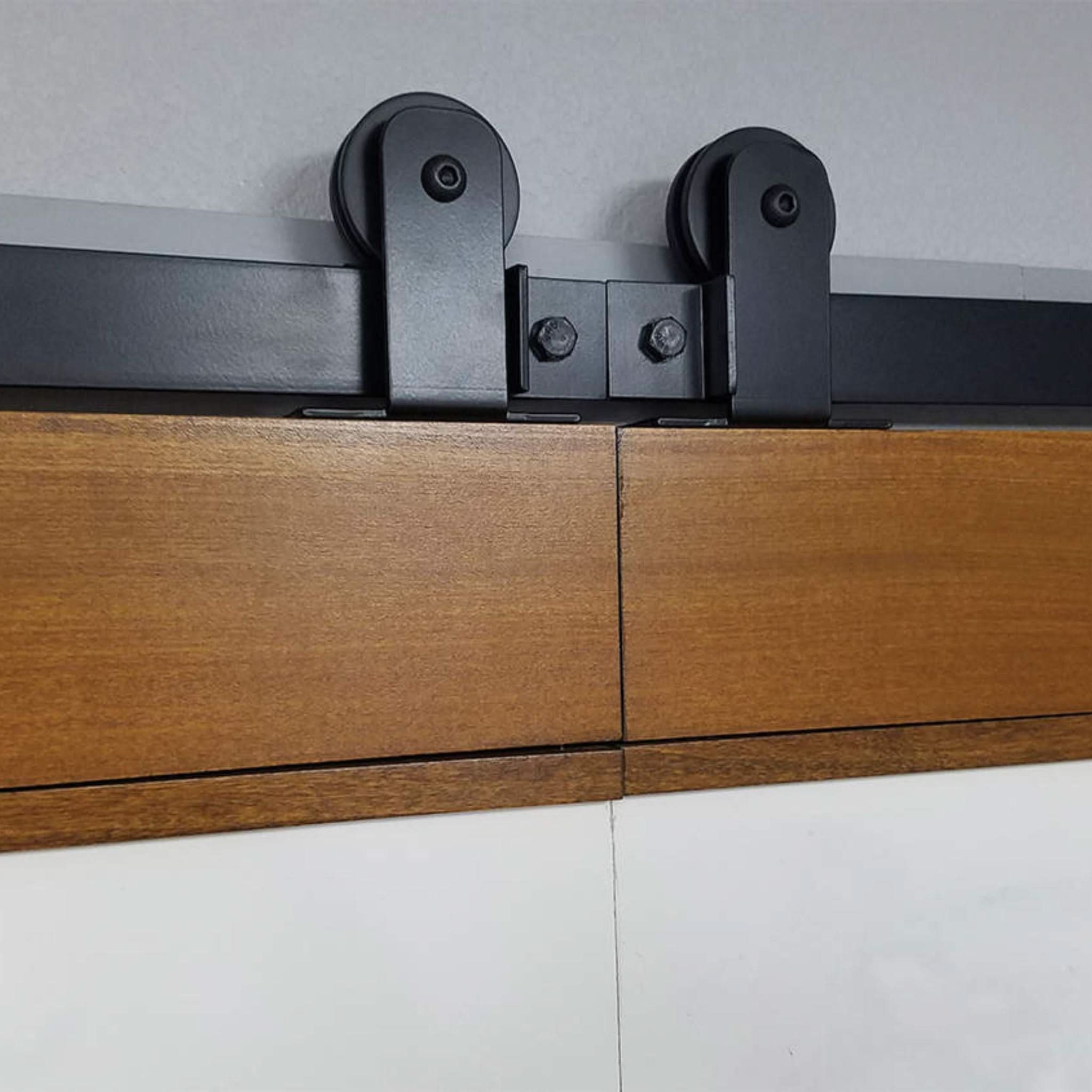 Close-up of Black Straight Top Mount Single Track barn door hardware installed on biparting wooden door panels.