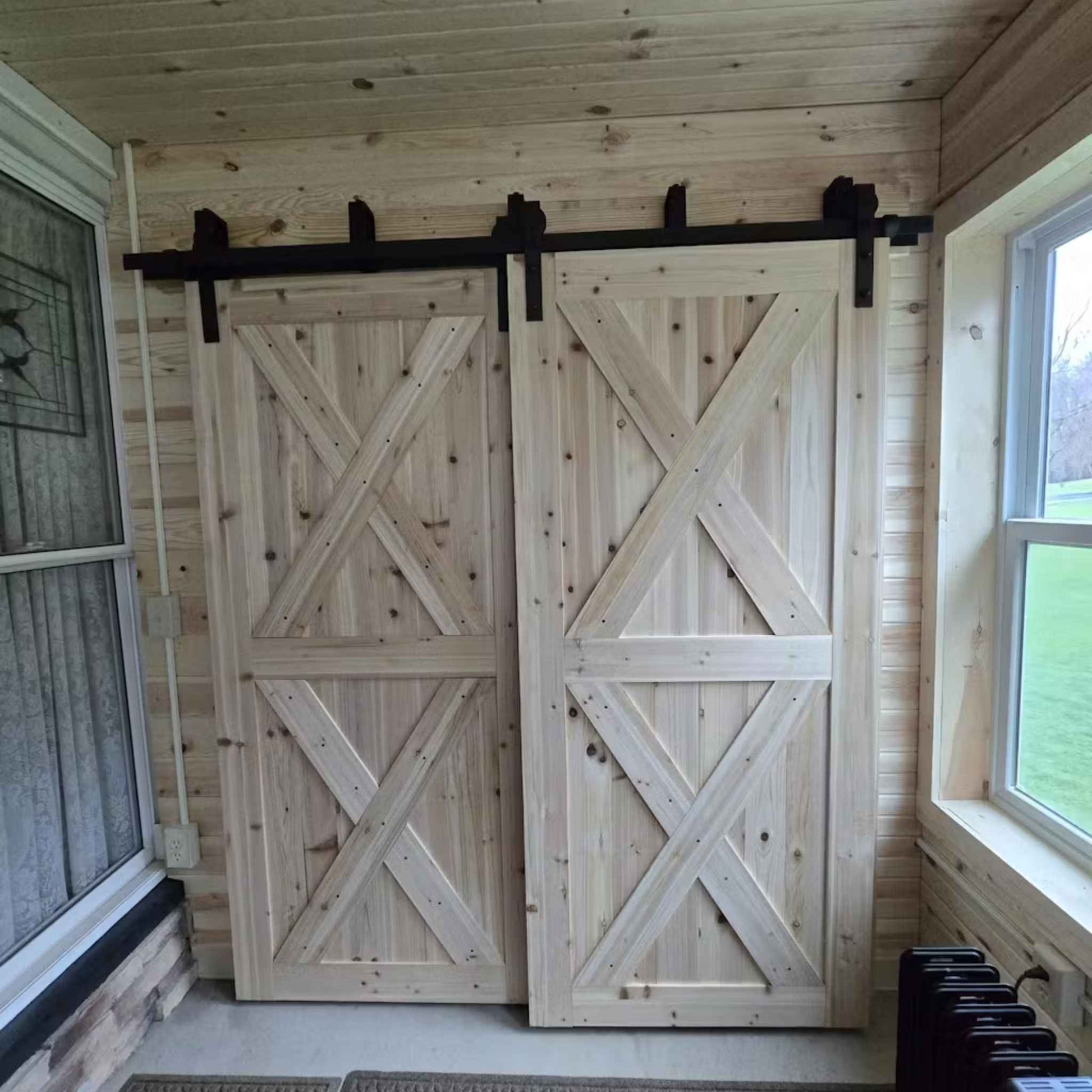 A customer install of a J-Strap double bypass barn door hardware kit in a matte black finish, shown on two sliding barn doors.