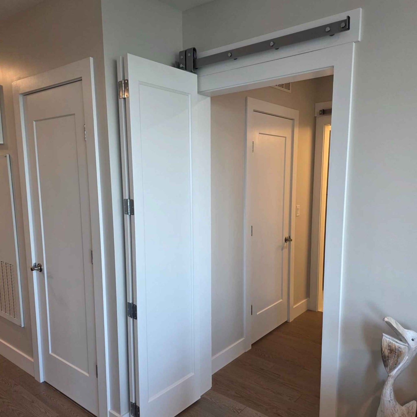 Customer installation photo of a white bifold door system running on our premium sliding barn door hardware with a modern, silver metallic finish.