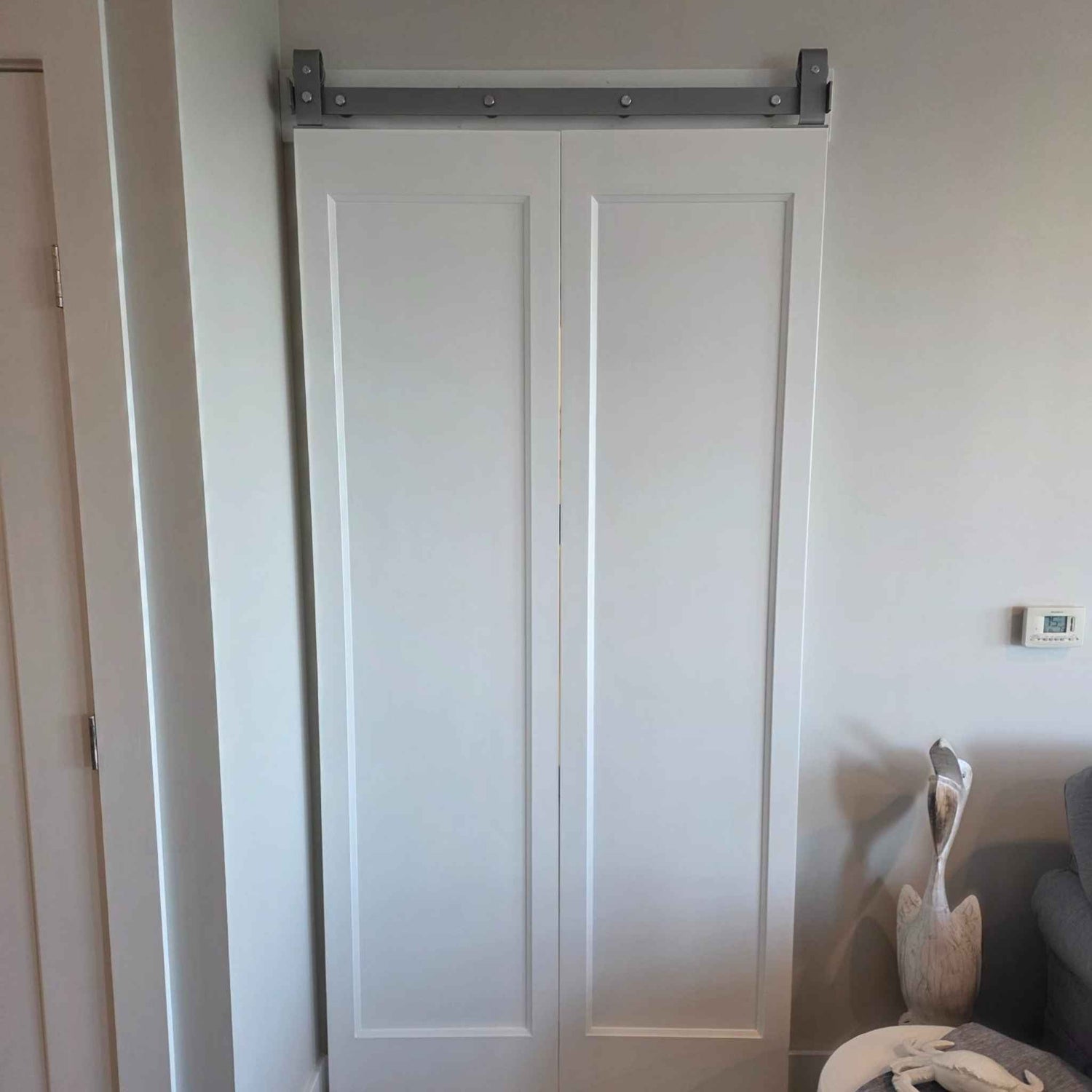 A J Top Mount bifold barn door hardware kit in a silver metallic finish on a 2-door system, installed in a customer's hallway.