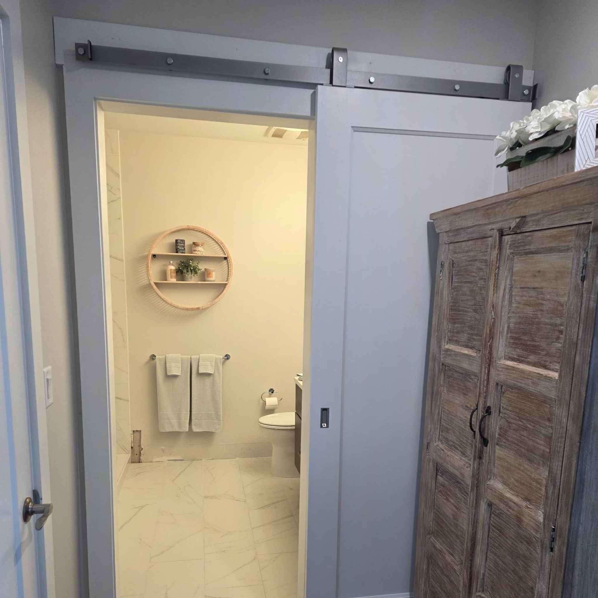 A J Top Mount single track barn door hardware kit in a silver metallic finish, installed for a customer's bathroom.