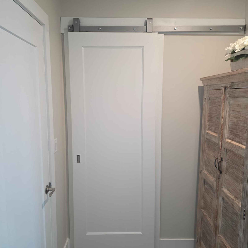 A J Top Mount single track barn door hardware kit in a silver metallic finish, installed for a customer's bathroom.