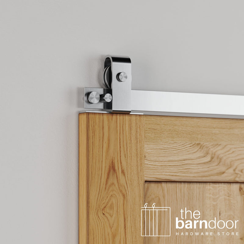 Close-up of Stainless Steel J Top Mount barn door hardware installed on the top edge of a natural wood door, highlighting the sleek, contemporary metal finish.