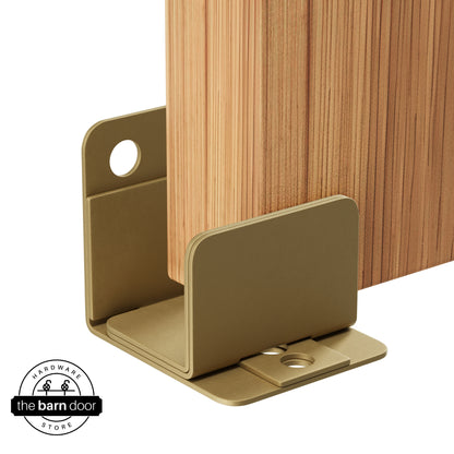 A gold U-shaped floor guide with a side plate, holding a light wood barn door in place.