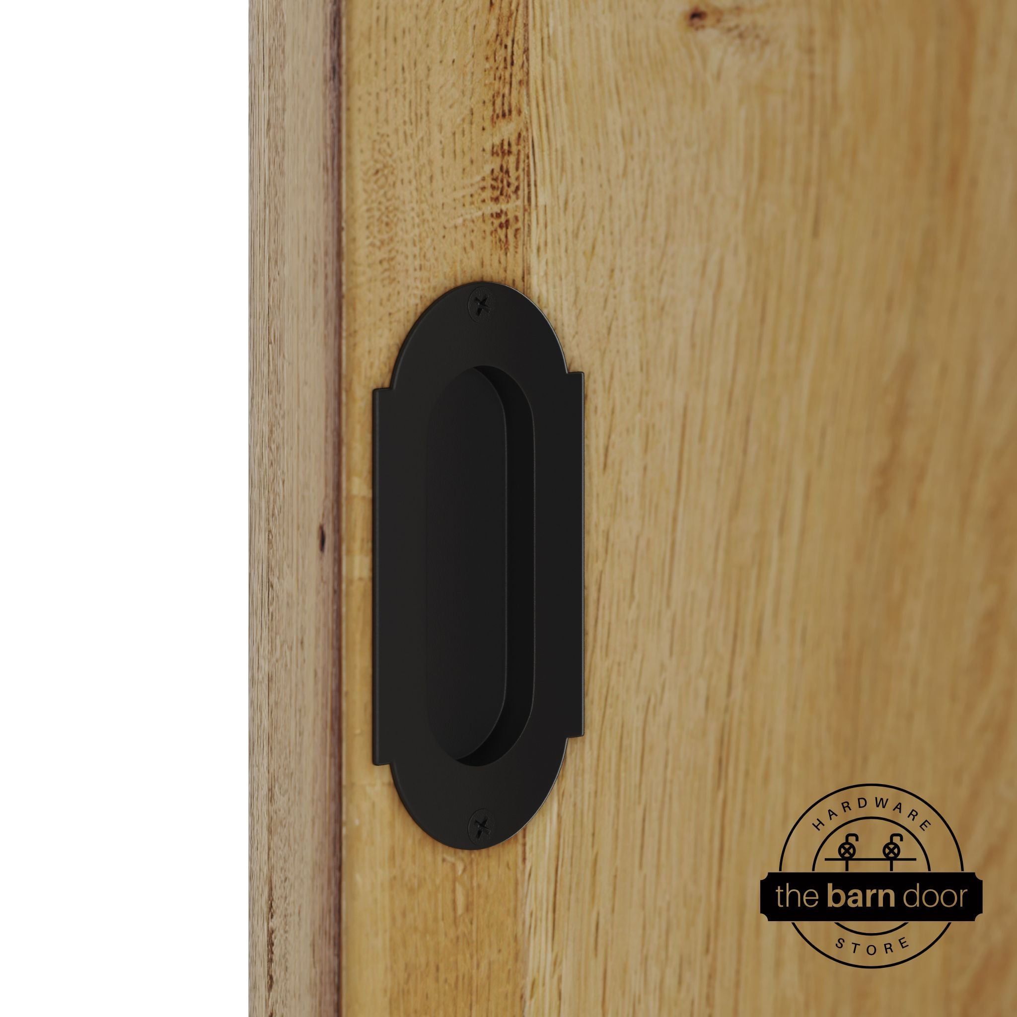 Matte black flush pull handle with full radius wings mounted on a light oak barn door, brushed silver finish with oval recessed grip and four mounting screws