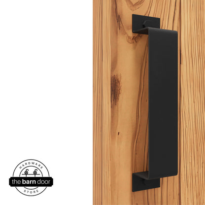 A matte black, arch-shaped barn door handle is mounted on a light-colored wooden door with a vertical grain pattern.
