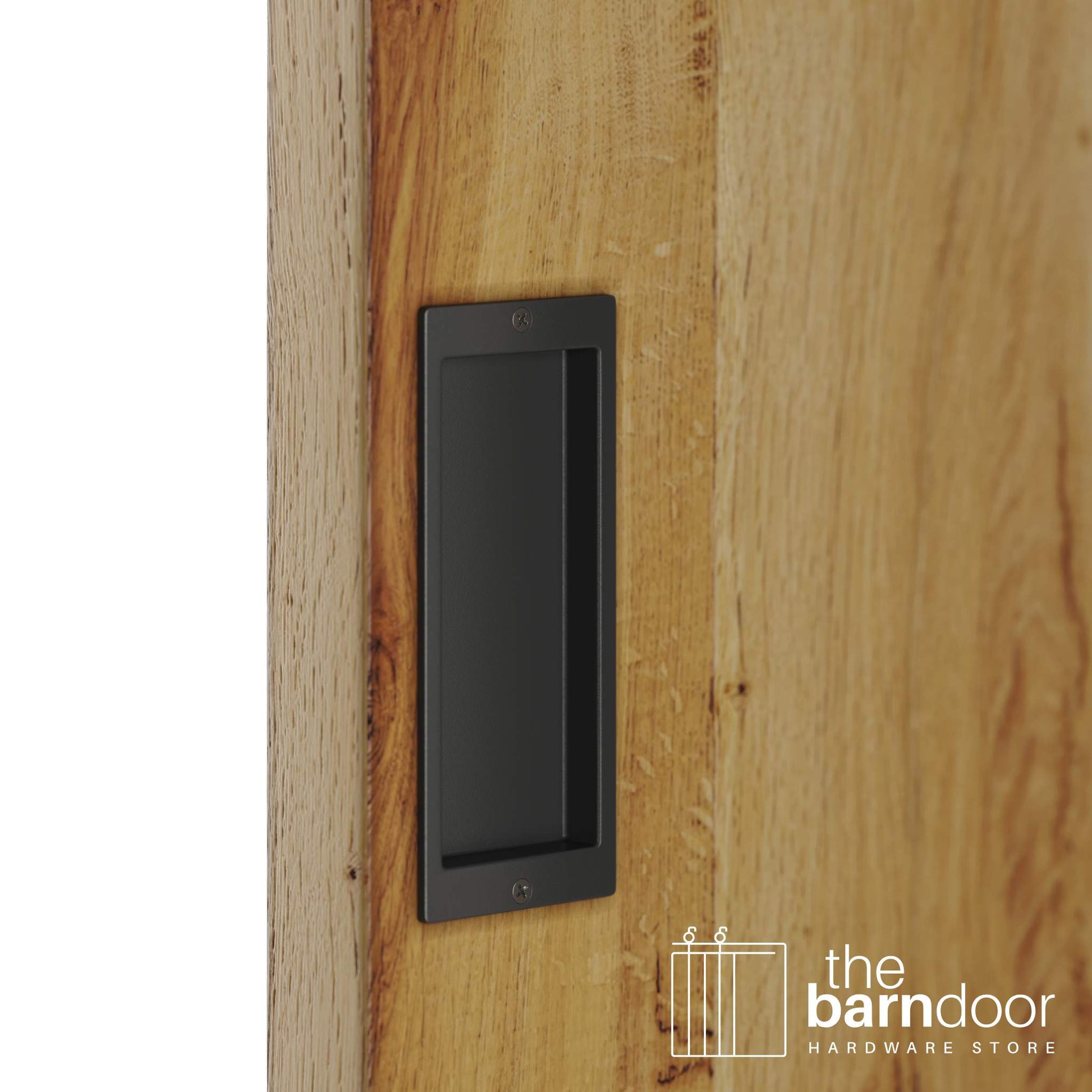 A close-up shot of a recessed rectangular flush pull handle in a matte black finish, installed on a light brown wooden barn door.