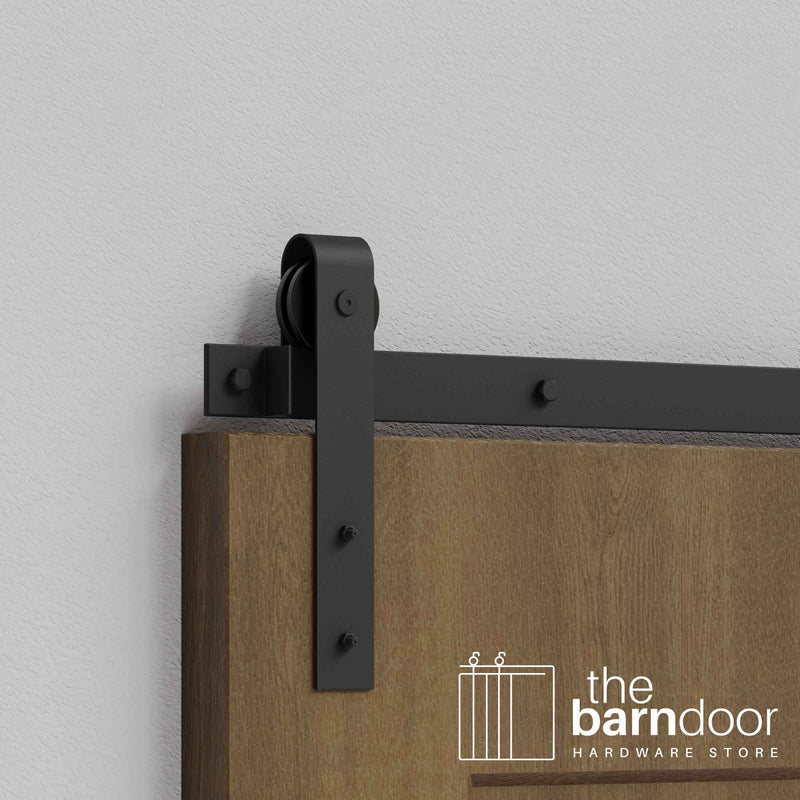 Close-up of Matte Black J-Strap Single Track barn door hardware installed on a wooden door panel.