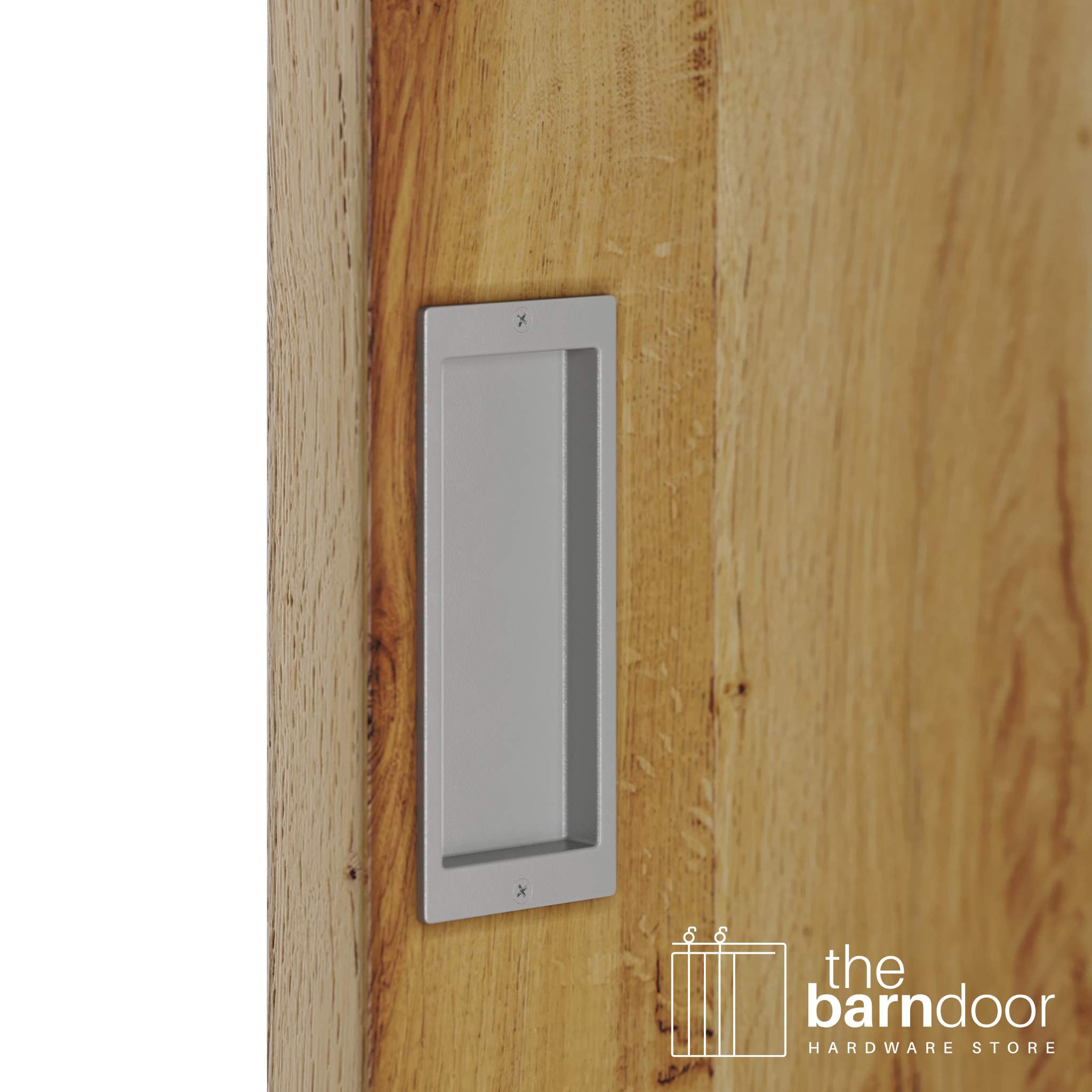 A close-up shot of a recessed rectangular flush pull handle in a PC Chrome finish, installed on a light brown wooden barn door.