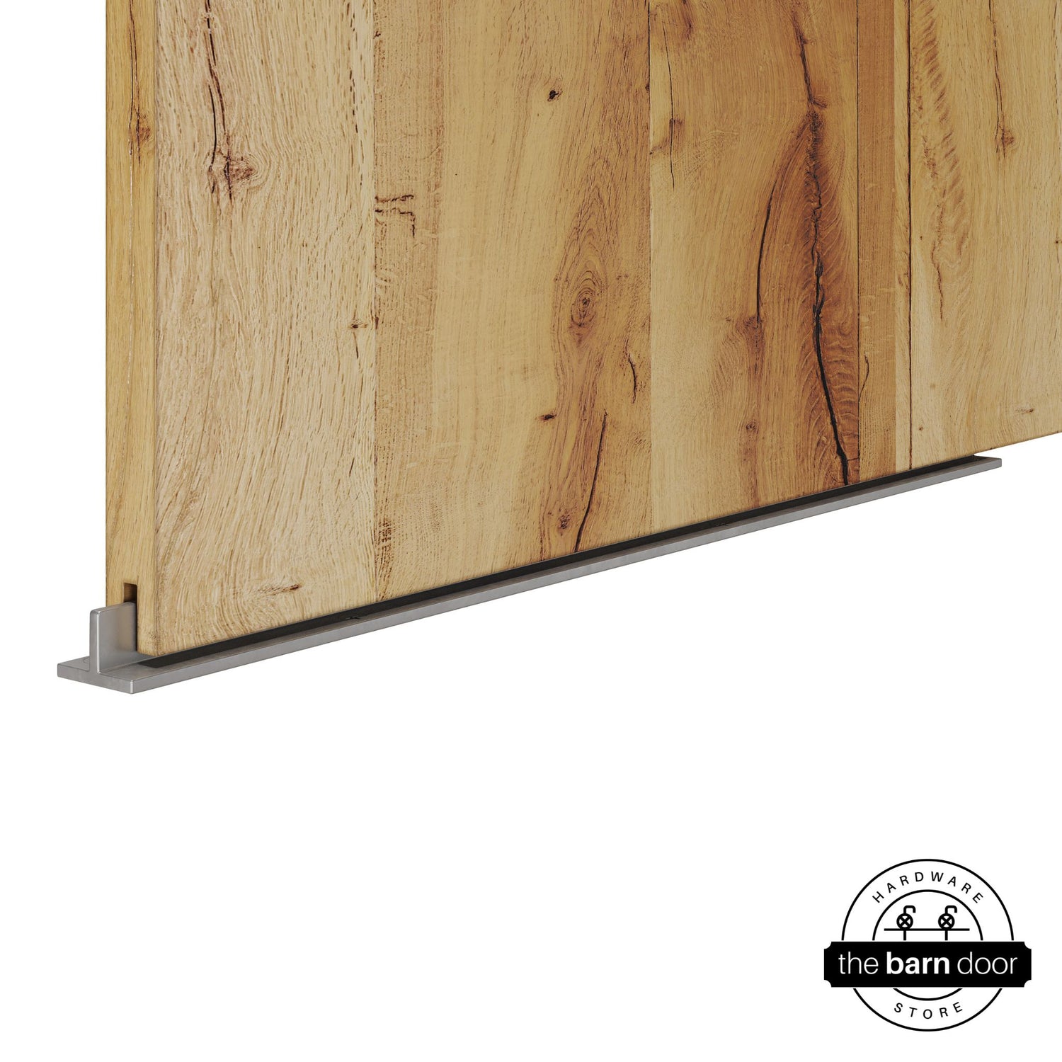 Raw steel continuous T-guide floor track for barn doors by The Barn Door Hardware Store. Close-up of a heavy-duty bottom floor guide installed on a rustic wood door for stabilization and smooth sliding operation.