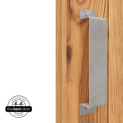 A raw steel, arch-shaped barn door handle is mounted on a light-colored wooden door with a vertical grain pattern.