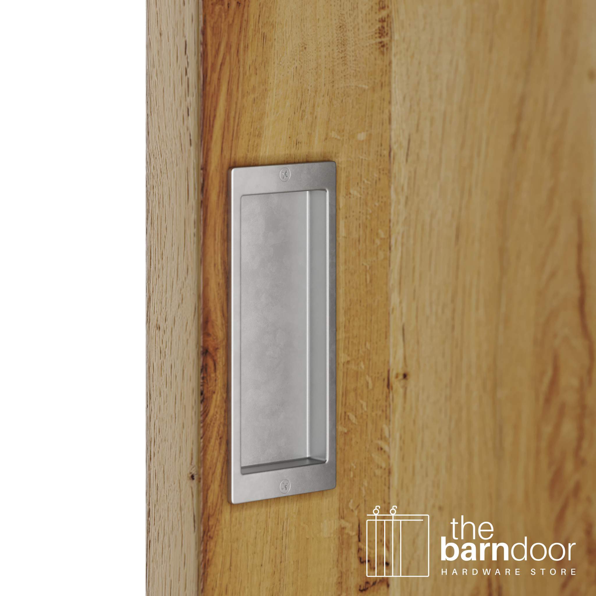 A close-up shot of a recessed rectangular flush pull handle in raw steel, installed on a light brown wooden barn door.