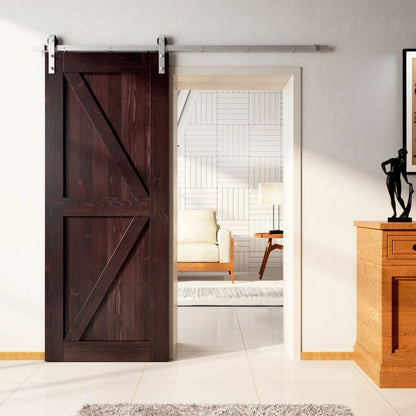 Rustic barn door with a Z-brace design in a deep red mahogany stain, installed with brushed nickel sliding hardware, partially revealing a living room with white tiled walls.