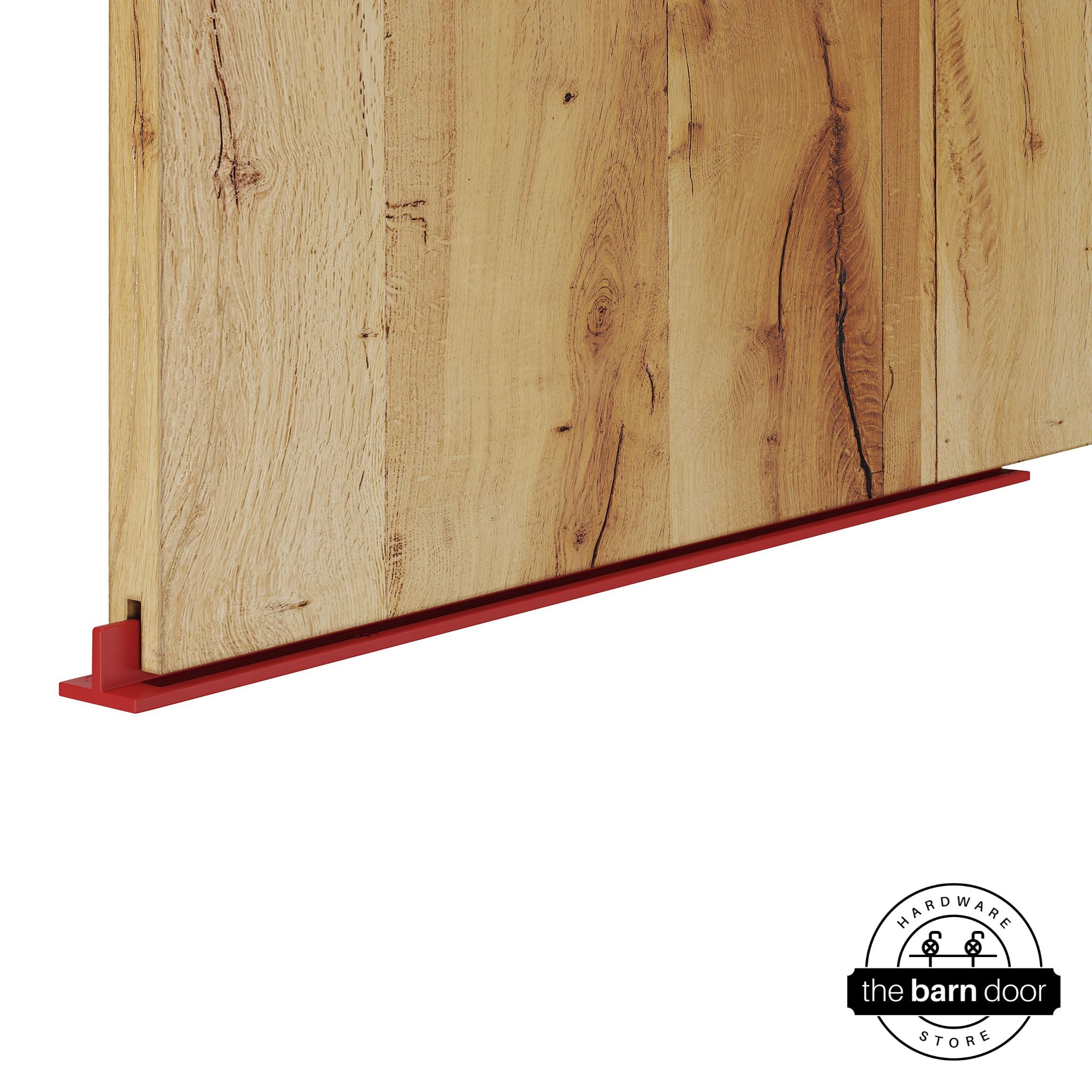 Regal Red continuous T-guide floor track for barn doors by The Barn Door Hardware Store. Close-up of a heavy-duty bottom floor guide installed on a rustic wood door for stabilization and smooth sliding operation.