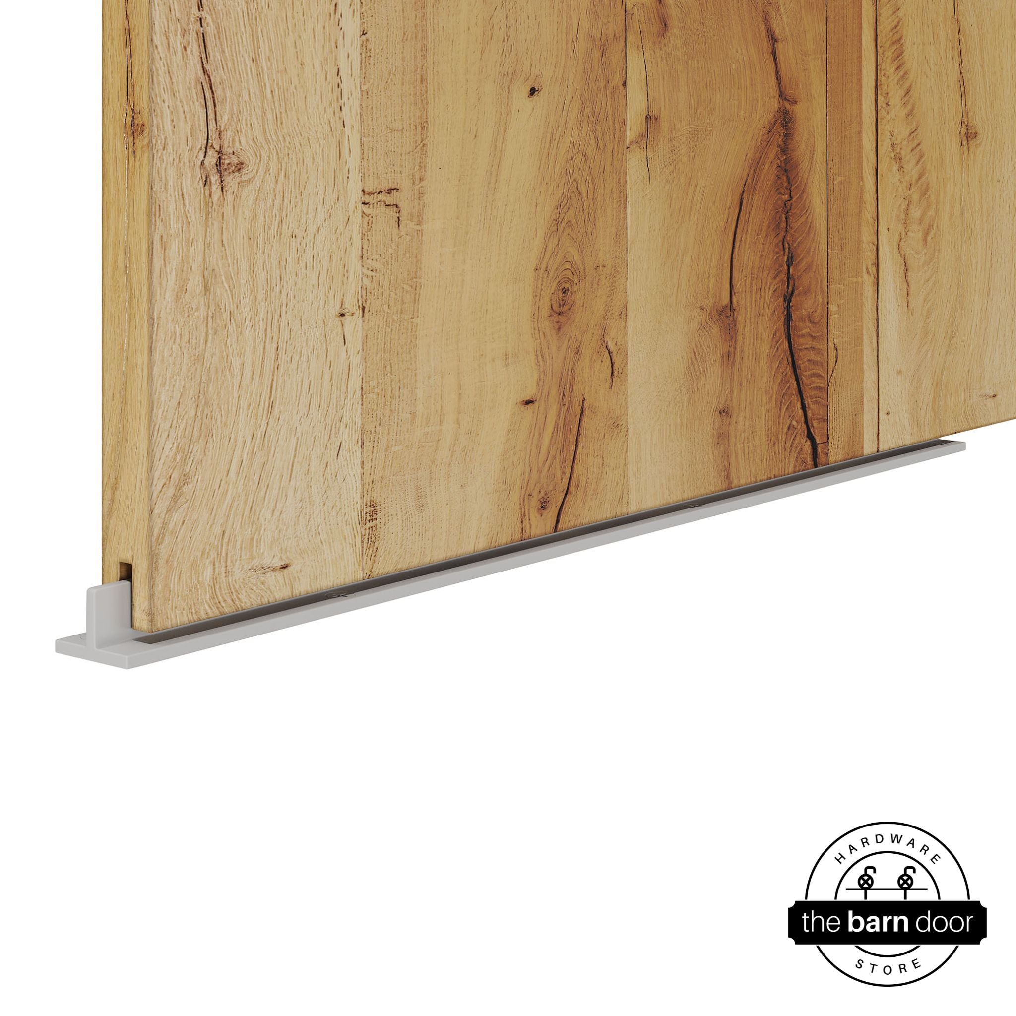 Rocket White continuous T-guide floor track for barn doors by The Barn Door Hardware Store. Close-up of a heavy-duty bottom floor guide installed on a rustic wood door for stabilization and smooth sliding operation.