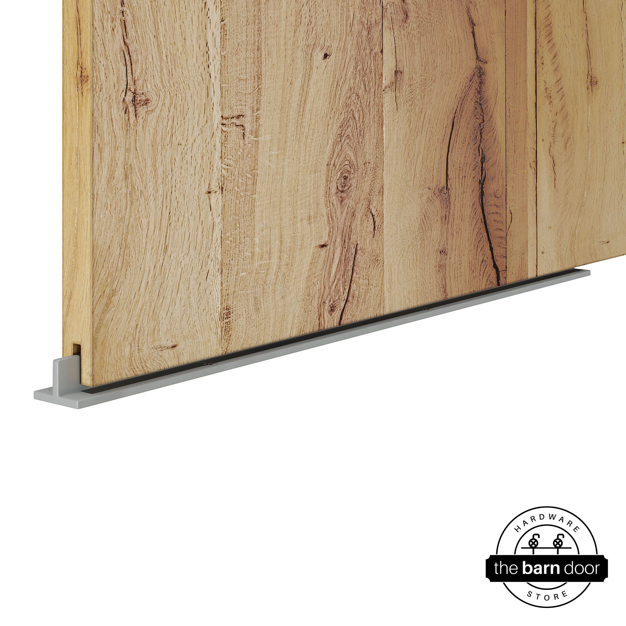 Silver Metallic continuous T-guide floor track for barn doors by The Barn Door Hardware Store. Close-up of a heavy-duty bottom floor guide installed on a rustic wood door for stabilization and smooth sliding operation.