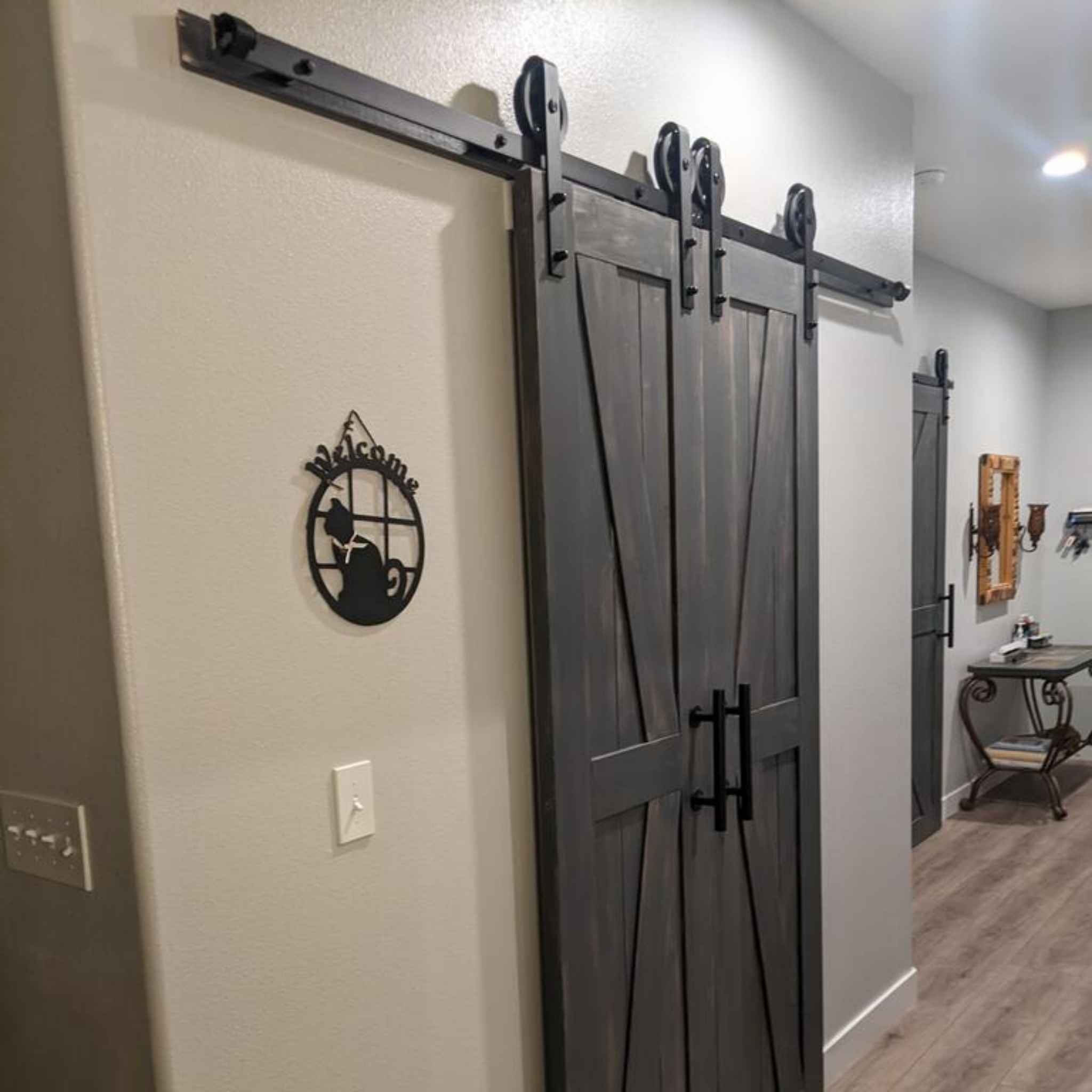 A customer install of a Spoke Wheel Single Track double door barn door hardware kit in a matte black finish, shown on a rustic wooden barn door.