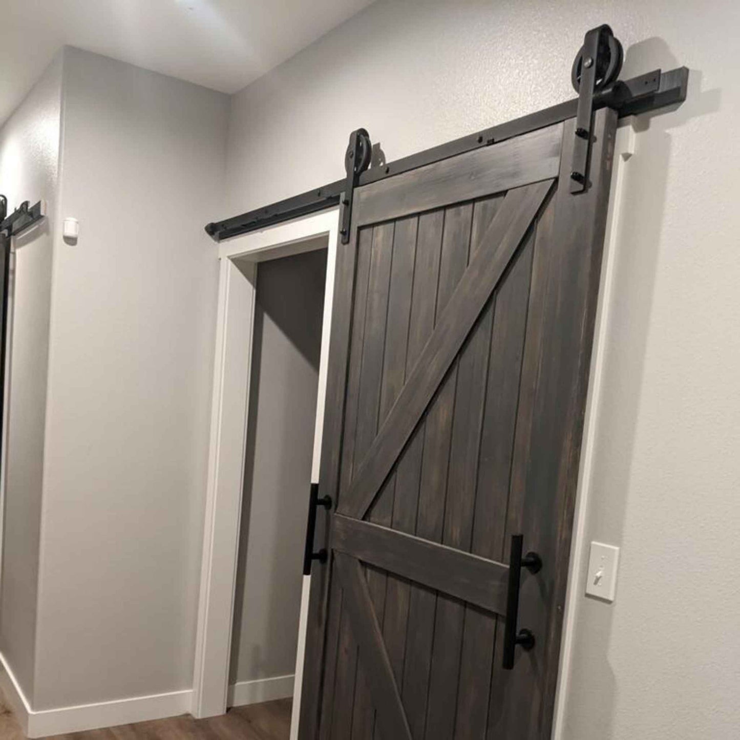 A customer install of a Spoke Wheel Single Track barn door hardware kit in a matte black finish, shown on a rustic wooden barn door.