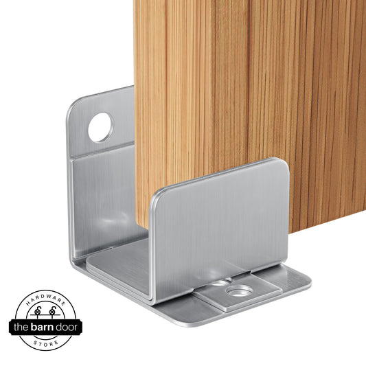 A polished stainless steel U-shaped floor guide, with a side plate, holds a light wood barn door in place.