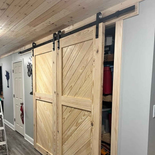 A customer install of a Straight Strap Single Track barn door hardware kit in a matte black finish, shown on a slanted wooden double barn doors.