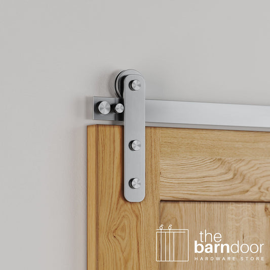 Close-up of Stainless Steel Straight Strap barn door hardware installed on a natural oak wood door, highlighting the modern, industrial strap design.