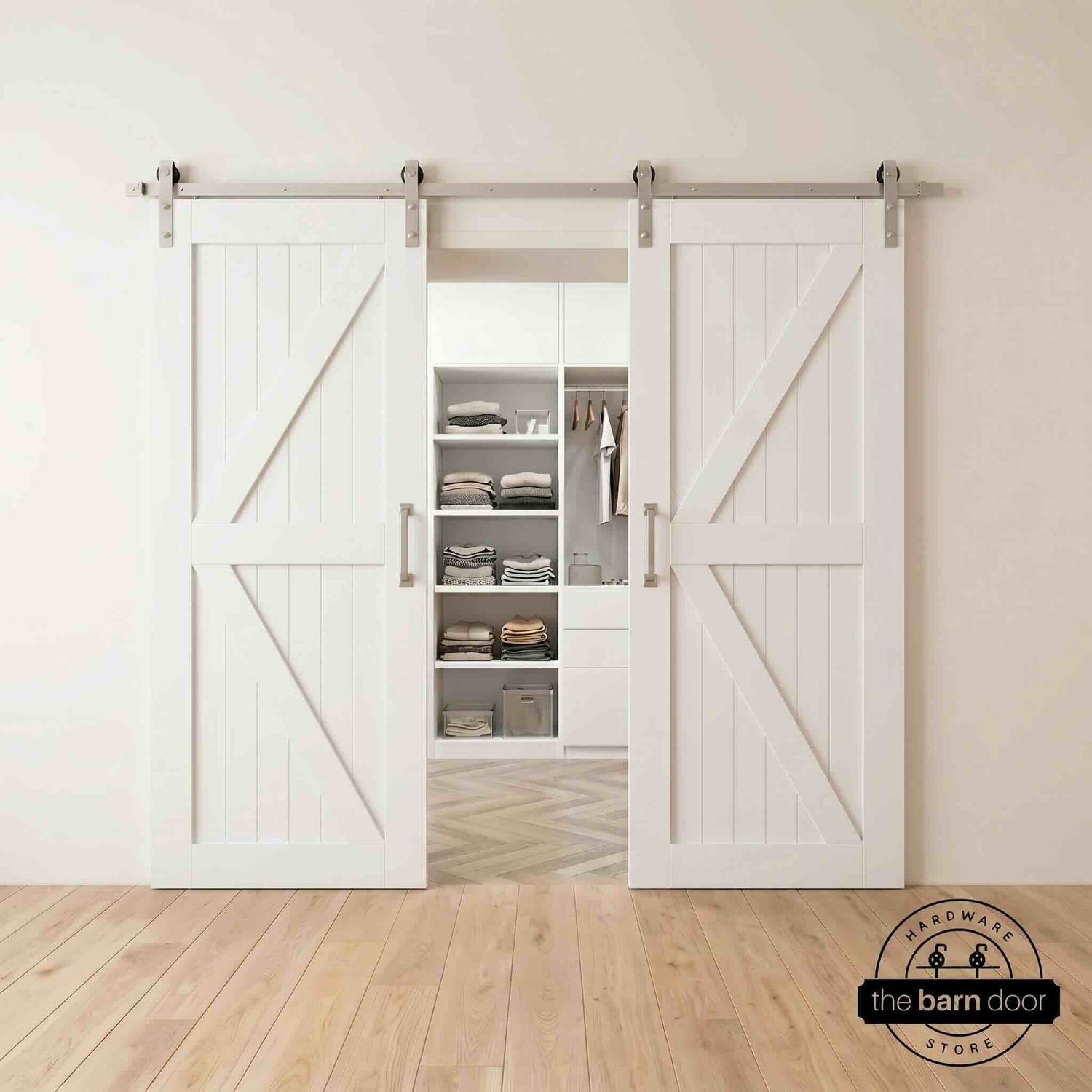 Two wood double barn doors with a two-panel vertical plank design in a white stain, installed with brushed nickel sliding hardware, partially revealing a living room area.