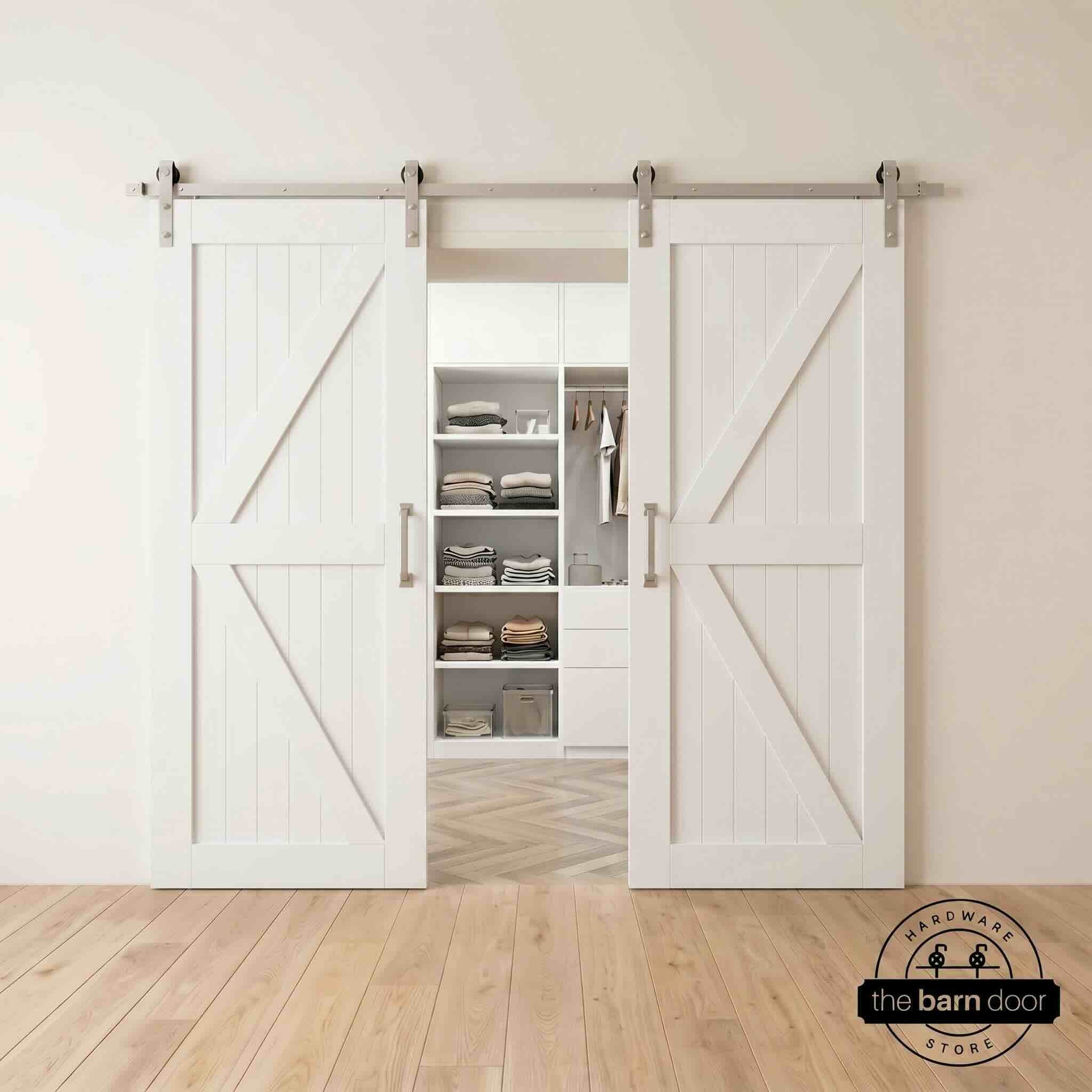 Two wood double barn doors with a two-panel vertical plank design in a white stain, installed with brushed nickel sliding hardware, partially revealing a living room area.