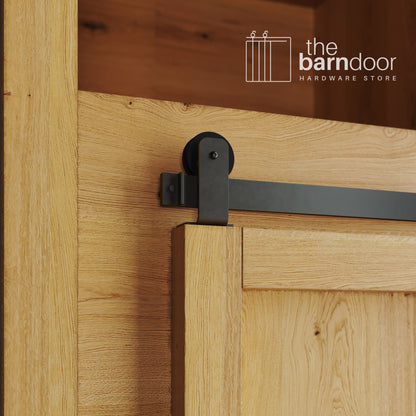 A close-up photograph of a sliding mini barn door on a natural oak cabinet, featuring arch-bronze top-mount straight hardware.