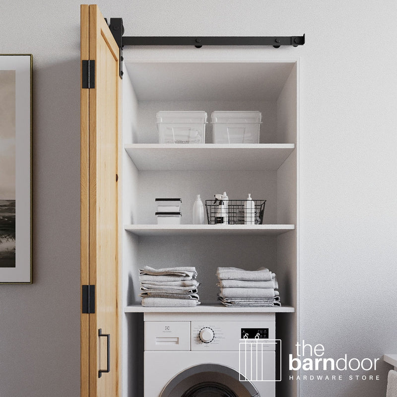 Open laundry room with shelves and a washer, featuring bifold barn door hardware.