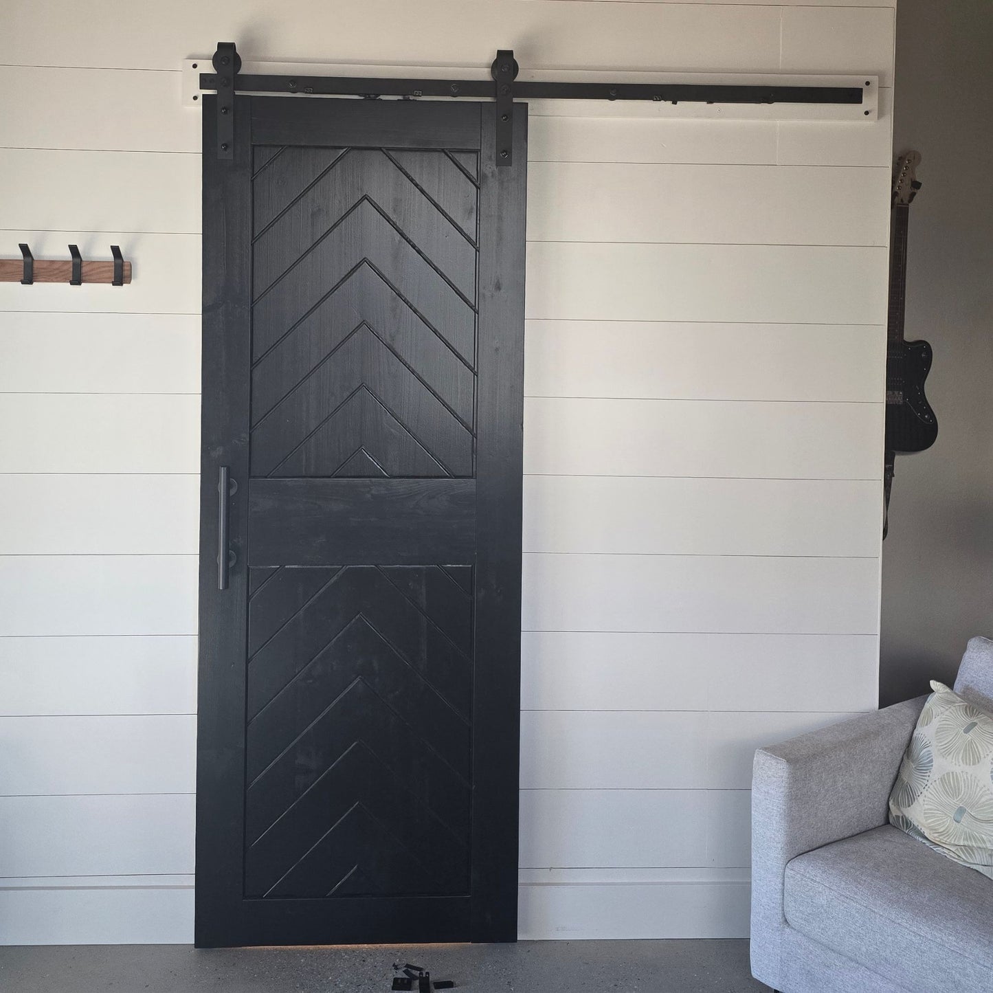 Barn door with chevron pattern in a room with a gray sofa and white wall.