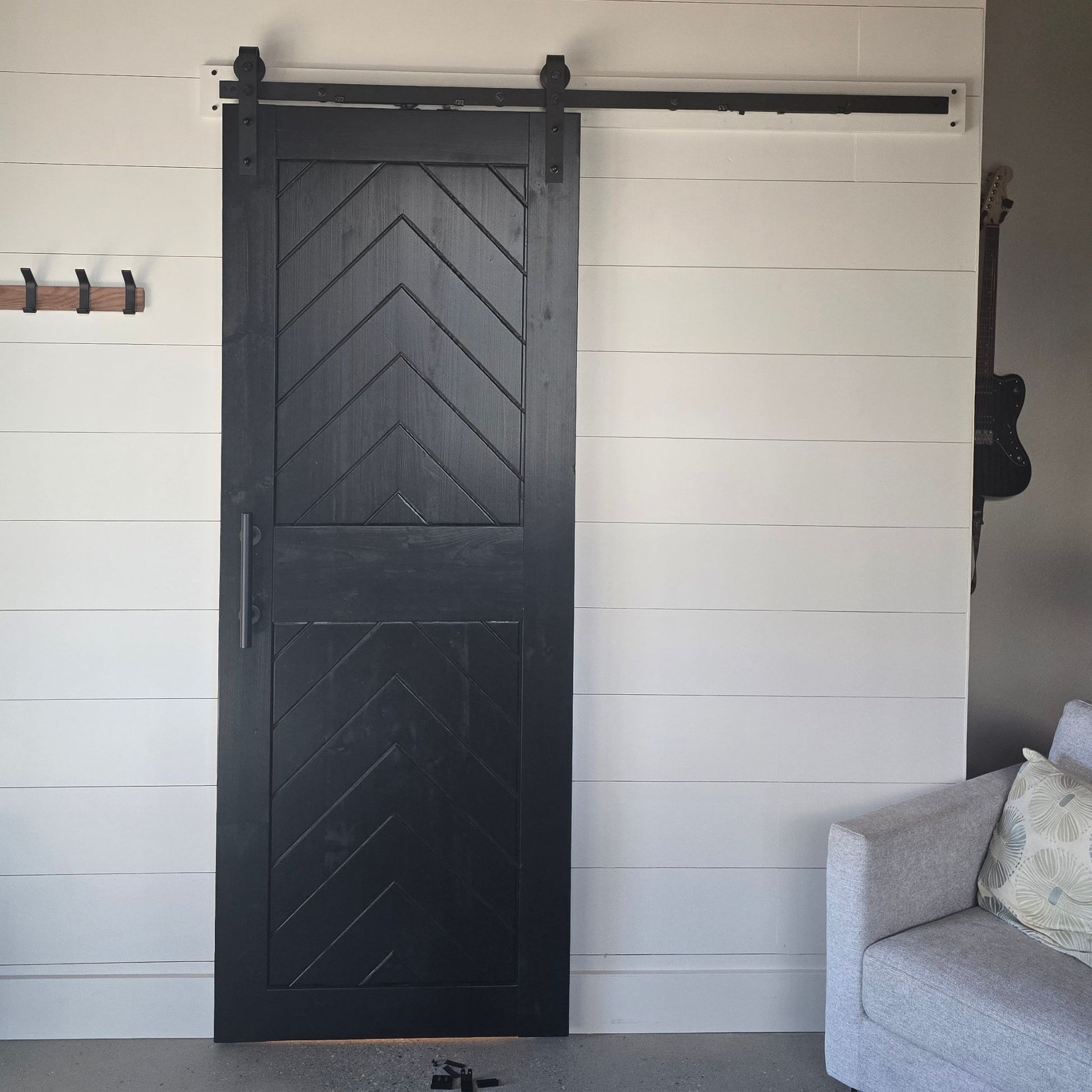 Barn door with chevron pattern in a room with a gray sofa and white wall.
