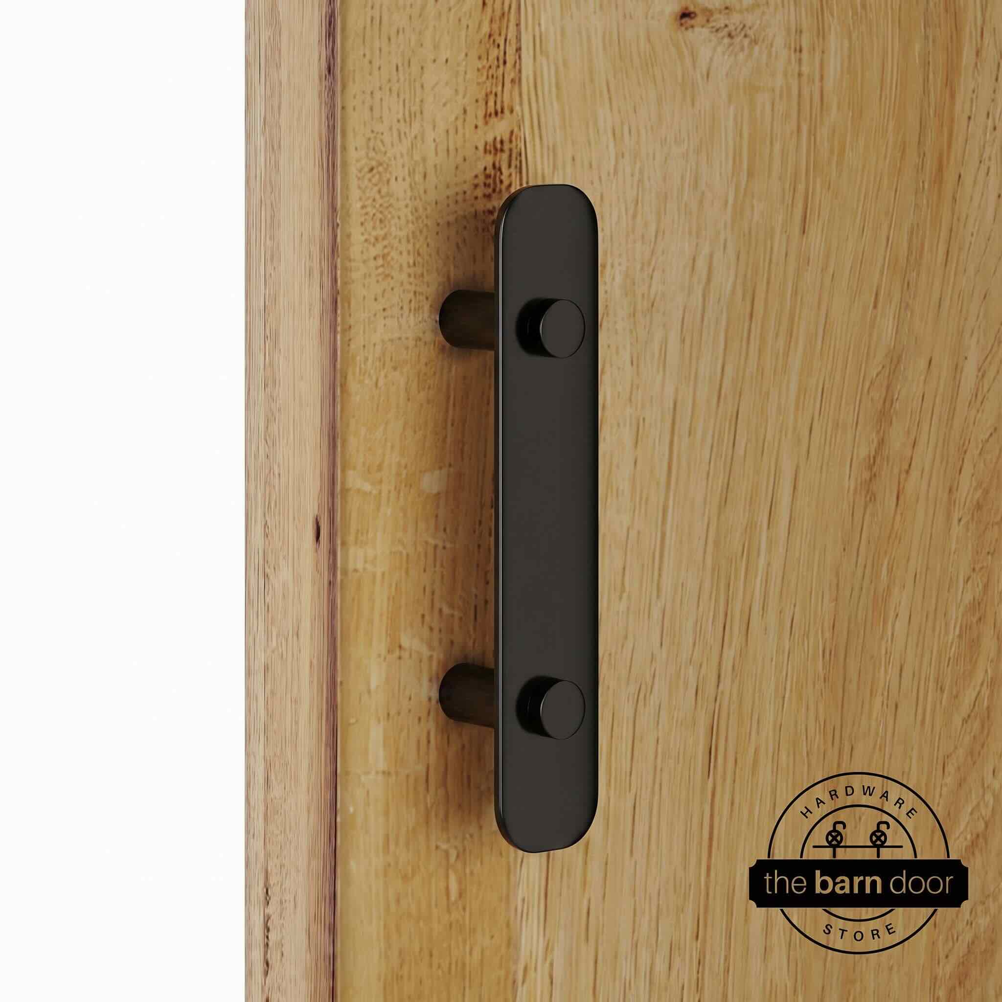 Black powder-coated stainless steel barn door flat bar pull handle on standoffs, mounted on a natural wood sliding barn door