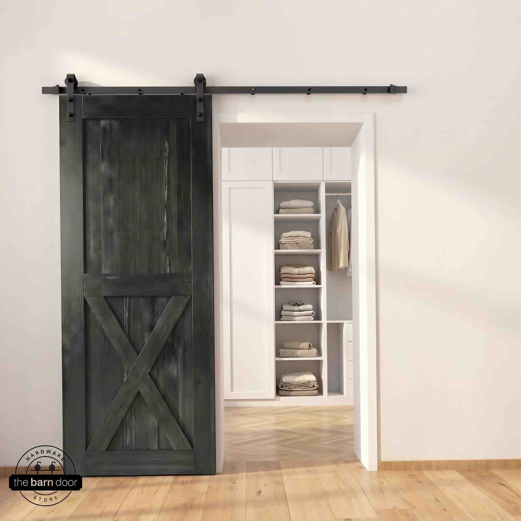 Half-X barn door in black stain finish with matte black sliding barn door hardware, open to a white built-in closet with herringbone hardwood floors