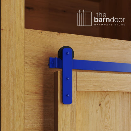 A close-up photograph of a natural oak cabinet with a sliding mini barn door, featuring a blue straight-strap hanger and a blue track system.