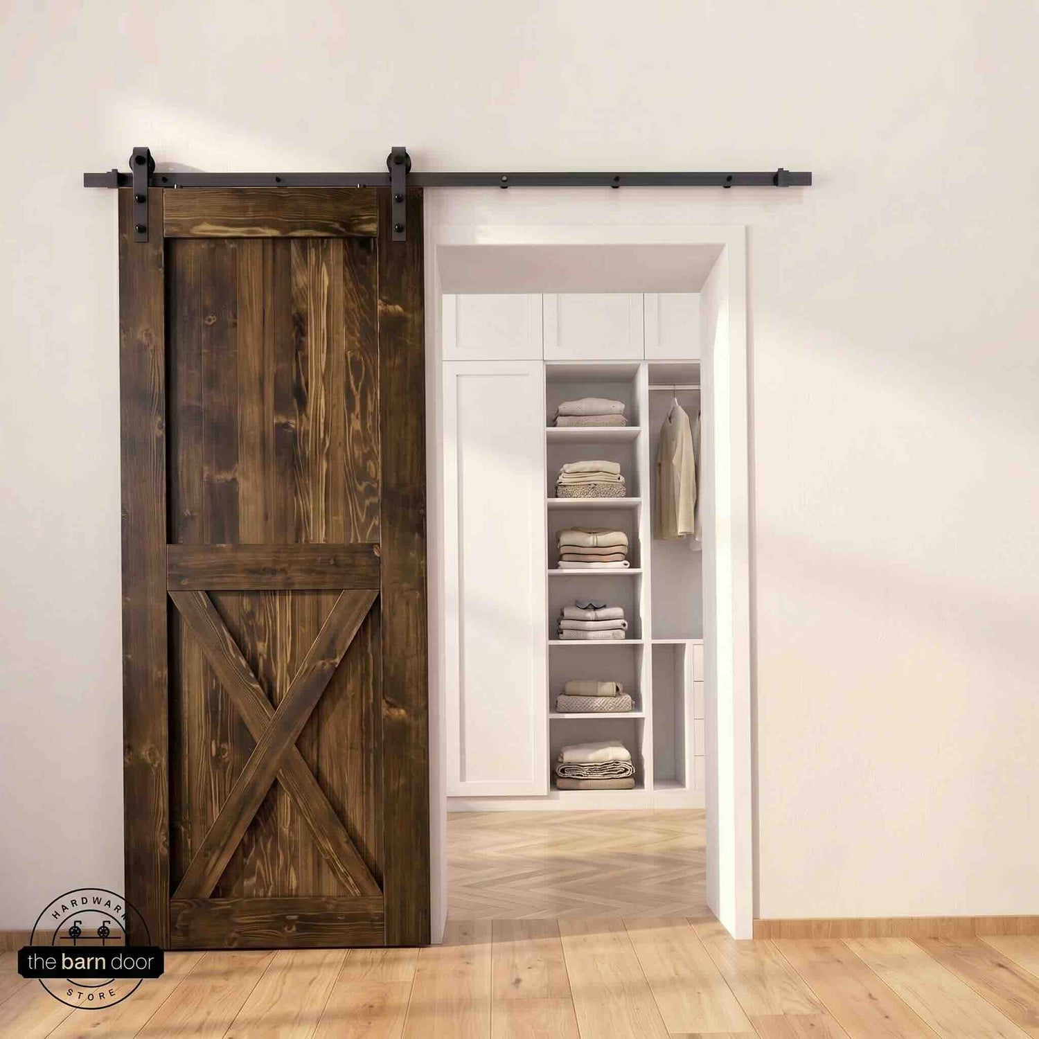 Half-X barn door in dark walnut stain finish with matte black sliding barn door hardware, open to a white built-in closet with herringbone hardwood floors